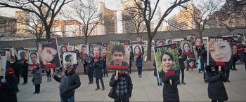 Movie still from “752 Is Not a Number” (2022), directed by Babak Payami – A group of people holding up signs with faces on them; Wide shot, High angle
