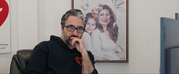 Movie still from “752 Is Not a Number” (2022), directed by Babak Payami – A man in front of a painting of a woman and a child; Close Up shot, Low angle