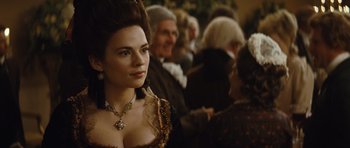 Movie still from “The Duchess” (2008), directed by Saul Dibb – A woman in a dress and a necklace is standing in front of a group of people; Close Up shot, Over the shoulder angle