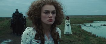 Movie still from “The Duchess” (2008), directed by Saul Dibb – Two women standing in a grassy field , one of whom is wearing a white dress; Close Up shot, Over the shoulder angle