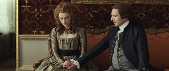 Movie still from “The Duchess” (2008), directed by Saul Dibb – A man and a woman sitting on a couch holding hands; Medium shot, Over the shoulder angle