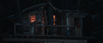 Movie still from “8-Bit Christmas” (2021), directed by Michael Dowse – A wooden structure with a tree in front of it at night time; Extreme Wide shot, Low angle