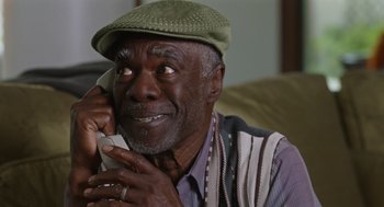 Movie still from “80 for Brady” (2023), directed by Kyle Marvin – An older man talking on a phone while wearing a hat; Close Up shot, High angle