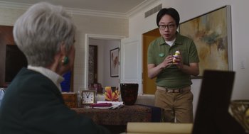 Movie still from “80 for Brady” (2023), directed by Kyle Marvin – A man standing in front of a table holding a bottle; Medium shot, Over the shoulder angle