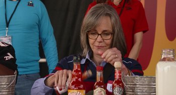 Movie still from “80 for Brady” (2023), directed by Kyle Marvin – A woman sitting at a table holding a hot sauce bottle; Close Up shot, Over the shoulder angle