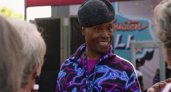 Movie still from “80 for Brady” (2023), directed by Kyle Marvin – A man in a purple jacket and a black hat; Close Up shot, Over the shoulder angle