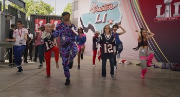 Movie still from “80 for Brady” (2023), directed by Kyle Marvin – A group of young people are dancing in front of an advertisement; Wide shot, High angle