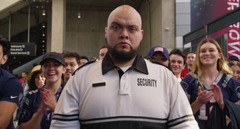 Movie still from “80 for Brady” (2023), directed by Kyle Marvin – A man that is wearing a security uniform; Medium shot, Low angle