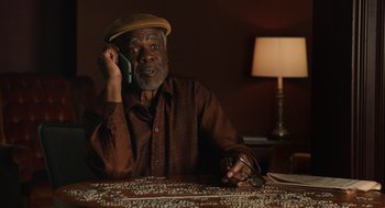 Movie still from “80 for Brady” (2023), directed by Kyle Marvin – An older man sitting at a table talking on a phone; Medium shot, High angle