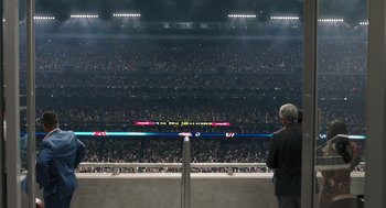 Movie still from “80 for Brady” (2023), directed by Kyle Marvin – A man standing in front of an audience at a sporting event; Extreme Wide shot, High angle