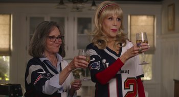 Movie still from “80 for Brady” (2023), directed by Kyle Marvin – Two women are holding wine glasses and posing for a picture; Medium shot, High angle