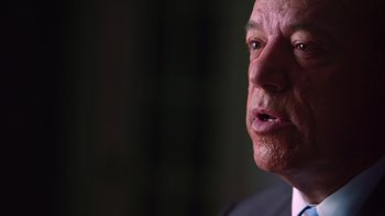 Movie still from “9/11: Inside the President's War Room” (2021), directed by Adam Wishart – An older man in a business suit looking at the camera; Close Up shot, Low angle