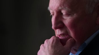 Movie still from “9/11: Inside the President's War Room” (2021), directed by Adam Wishart – An older man is looking pensive while holding his hand to his chin; Extreme Close Up shot, Over the shoulder angle