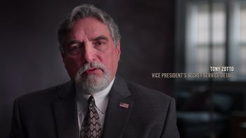 Movie still from “9/11: Inside the President's War Room” (2021), directed by Adam Wishart – A person wearing a suit and tie; Close Up shot, High angle