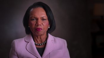 Movie still from “9/11: Inside the President's War Room” (2021), directed by Adam Wishart – An older woman wearing a pink jacket and a black necklace; Close Up shot, Low angle
