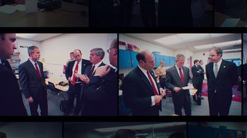 Movie still from “9/11: Inside the President's War Room” (2021), directed by Adam Wishart – A group of men in suits standing next to each other in a room; Medium shot, Over the shoulder angle