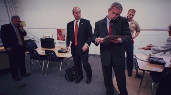 Movie still from “9/11: Inside the President's War Room” (2021), directed by Adam Wishart – A man in a suit and tie standing next to another man in a suit and tie; Medium shot, Over the shoulder angle