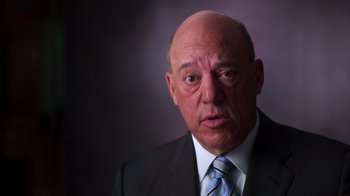 Movie still from “9/11: Inside the President's War Room” (2021), directed by Adam Wishart – An older bald man in a suit and tie; Close Up shot, Low angle