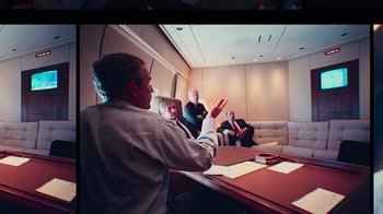 Movie still from “9/11: Inside the President's War Room” (2021), directed by Adam Wishart – A group of people sitting at a table in a room; Medium shot, Over the shoulder angle