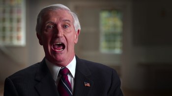 Movie still from “9/11: Inside the President's War Room” (2021), directed by Adam Wishart – An older man wearing a suit and tie with his mouth wide open; Close Up shot, Low angle