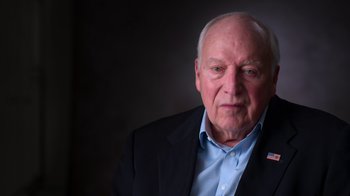 Movie still from “9/11: Inside the President's War Room” (2021), directed by Adam Wishart – An older man wearing a jacket and a blue shirt; Close Up shot, Low angle