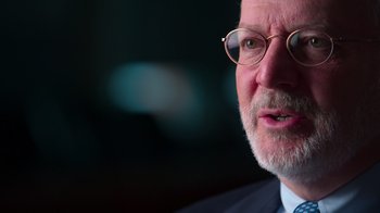 Movie still from “9/11: Inside the President's War Room” (2021), directed by Adam Wishart – An older man wearing glasses and wearing a suit; Close Up shot, Over the shoulder angle