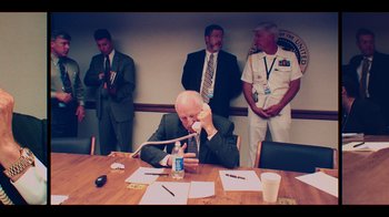 Movie still from “9/11: Inside the President's War Room” (2021), directed by Adam Wishart – An older man sitting at a conference table talking on the phone; Medium shot, High angle