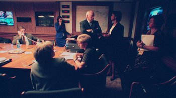 Movie still from “9/11: Inside the President's War Room” (2021), directed by Adam Wishart – A group of people sitting around a table in a room; Medium shot, Over the shoulder angle