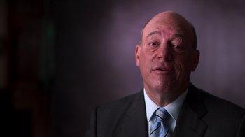 Movie still from “9/11: Inside the President's War Room” (2021), directed by Adam Wishart – An older man in a suit and tie looking at the camera; Close Up shot, Low angle