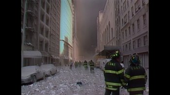 Movie still from “9/11: Inside the President's War Room” (2021), directed by Adam Wishart – A group of firemen standing in the middle of a street; Wide shot, High angle