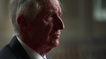 Movie still from “9/11: Inside the President's War Room” (2021), directed by Adam Wishart – An older man in a suit looking to his left; Close Up shot, Low angle