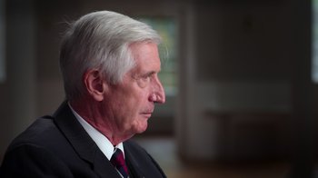 Movie still from “9/11: Inside the President's War Room” (2021), directed by Adam Wishart – An older man wearing a suit and a red neck tie; Close Up shot, Over the shoulder angle