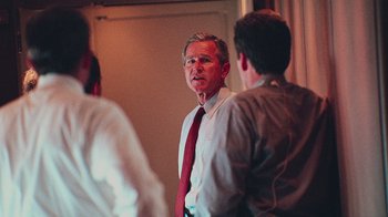 Movie still from “9/11: Inside the President's War Room” (2021), directed by Adam Wishart – A man wearing a red tie talking to two other men; Medium shot, Over the shoulder angle