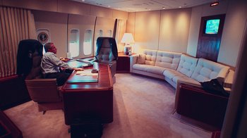 Movie still from “9/11: Inside the President's War Room” (2021), directed by Adam Wishart – A man sitting at a desk inside of an airplane; Wide shot, High angle