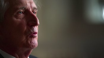 Movie still from “9/11: Inside the President's War Room” (2021), directed by Adam Wishart – An older man with white hair looking to his left; Extreme Close Up shot, Over the shoulder angle