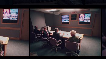 Movie still from “9/11: Inside the President's War Room” (2021), directed by Adam Wishart – A group of people sitting at a table in front of a television; Wide shot, High angle