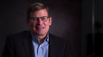 Movie still from “9/11: Inside the President's War Room” (2021), directed by Adam Wishart – A person wearing glasses and a suit; Close Up shot, Low angle