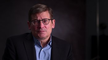 Movie still from “9/11: Inside the President's War Room” (2021), directed by Adam Wishart – A person wearing glasses and a suit; Close Up shot, Low angle