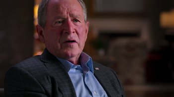 Movie still from “9/11: Inside the President's War Room” (2021), directed by Adam Wishart – An older man wearing a jacket and a blue shirt; Close Up shot, Over the shoulder angle