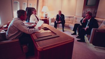 Movie still from “9/11: Inside the President's War Room” (2021), directed by Adam Wishart – A group of people sitting around a table in an airplane; Wide shot, High angle