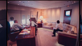 Movie still from “9/11: Inside the President's War Room” (2021), directed by Adam Wishart – Three men sitting at a table in a room with a couch; Wide shot, High angle