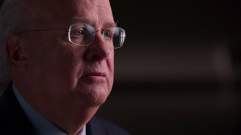 Movie still from “9/11: Inside the President's War Room” (2021), directed by Adam Wishart – An older man wearing glasses and a suit; Close Up shot, Over the shoulder angle