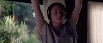 Movie still from “A Banquet” (2021), directed by Ruth Paxton – A young girl wearing headphones while sitting in a chair; Close Up shot, Low angle