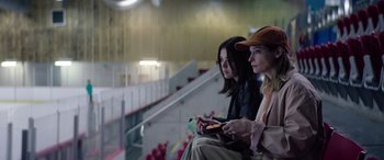 Movie still from “A Banquet” (2021), directed by Ruth Paxton – Two women are sitting on a bleacher and one is holding a cell phone; Medium shot, Low angle