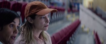 Movie still from “A Banquet” (2021), directed by Ruth Paxton – A woman wearing a baseball cap sitting in a stadium; Close Up shot, High angle