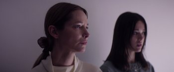 Movie still from “A Banquet” (2021), directed by Ruth Paxton – A woman is looking into the distance while another woman looks on in the background; Close Up shot, Low angle