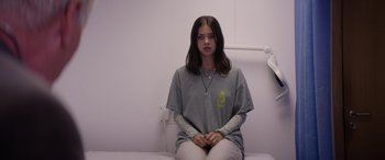 Movie still from “A Banquet” (2021), directed by Ruth Paxton – A woman sitting on a bed in a room; Medium shot, Low angle