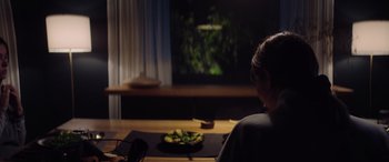 Movie still from “A Banquet” (2021), directed by Ruth Paxton – A person sitting at a table watching television; Close Up shot, Over the shoulder angle