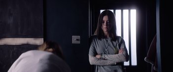 Movie still from “A Banquet” (2021), directed by Ruth Paxton – A woman standing with her arms crossed in front of a door; Medium shot, Over the shoulder angle