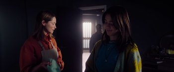 Movie still from “A Banquet” (2021), directed by Ruth Paxton – Two young women standing in a dark room; Medium shot, Over the shoulder angle